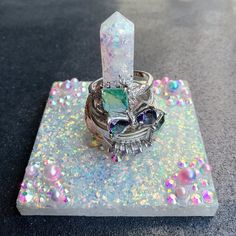 a diamond ring sitting on top of a piece of glass with beads and crystals around it