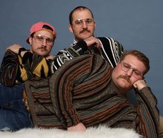 three men laying on the floor with one man wearing glasses and another in a sweater