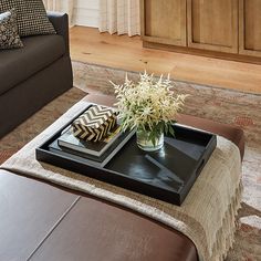 a living room with a couch, coffee table and ottoman in the center piece is a tray with flowers on it