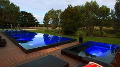 an outdoor swimming pool with wooden decking and large blue glass pools surrounded by trees