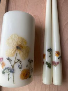 two white candles with flowers painted on them next to each other and one candle holder