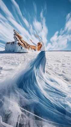 a woman is standing in the middle of an icy field with mountains and clouds behind her