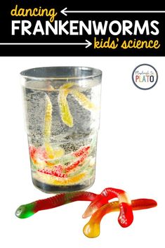 a glass filled with jelly worms next to a red and green plastic worm toy on top of a white background