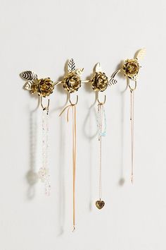 five different necklaces hanging from hooks on a white wall with beads and leaves attached to them