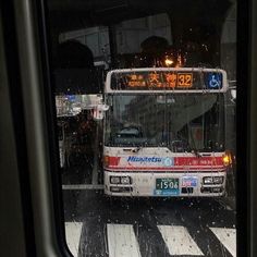 a bus driving down a street next to a cross walk in the rain with it's lights on