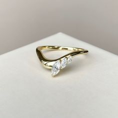 a gold ring with three pear shaped diamonds on the side, sitting on top of a white surface