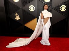 a woman in a white gown and cape on the red carpet at an awards event