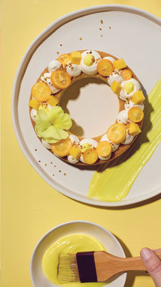 a person holding a paintbrush near a cake on a plate with oranges and cream