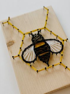 a string art insect sitting on top of a wooden board