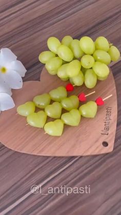 there is a heart shaped cutting board with grapes on it and flowers next to it