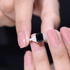 a woman's hand holding a ring with a black stone on it and diamond accents