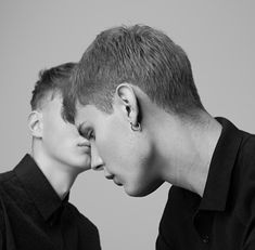 two young men standing next to each other with their faces close together, one is touching the other's ear