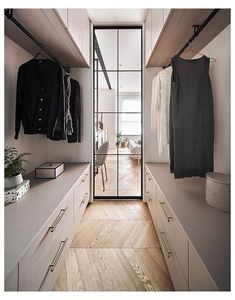 a walk - in closet with white cabinets and wooden flooring, open glass doors leading to the bedroom