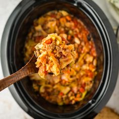 a wooden spoon full of food in a crock pot with meat and vegetables on top