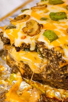 a close up of a piece of food with cheese and vegetables on it, sitting on foil