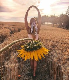 a woman in a sunflower skirt standing in a field with her hands up above her head