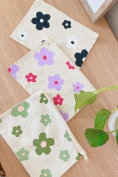 three flowered pouches sitting on top of a wooden table next to a plant