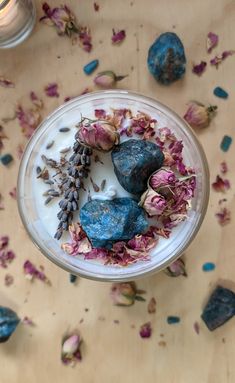 a bowl filled with rocks and flowers on top of a table next to a candle