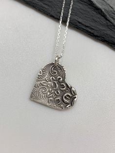 This floral silver heart necklace has been entirely handmade using .999 fine silver. It has been cut from fine silver precious metal clay, textured, fired and oxidized. The pendant hangs from a sterling silver diamond cut cable chain. This fine silver pendant features an embossed lovely rose textured print. Pendant size: approximately 3/4 x 3/4 inches Chain length: adjustable at 16 and 18 inches can also be customized to whatever length needed The necklace is sent in a gift box. This jewelry can Unique Etched Sterling Silver Necklace, Artisan Engraved Necklaces For Anniversary, Etched Sterling Silver Necklace Gift, Etched Sterling Silver Necklace For Gift, Unique Engraved Necklaces For Anniversary, Sterling Silver Etched Necklace For Gift, Artisan Engraved Heart Jewelry, Unique Engraved Necklace For Anniversary, Artisan Engraved Heart-shaped Jewelry