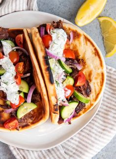 two tacos with meat, tomatoes, cucumbers and onions on a plate