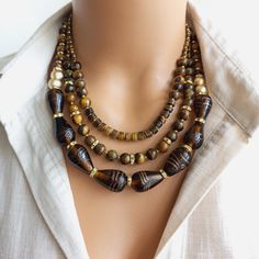 This exquisite piece perfectly combines vibrant Indian glass beads with the earthy allure of Tiger Eye natural stones. Each bead is meticulously handcrafted, showcasing the rich cultural heritage of India. The warm hues of the Tiger Eye stones create a captivating contrast against the intricately designed glass beads, making this necklace a true statement piece. With its adjustable length and secure clasp, it can be easily customized to fit any neckline. Whether you're heading to a special event Gold Beaded Necklaces With Natural Stones And Czech Glass, Brown Glass Beads For Jewelry Making, Oval Glass Gemstone Beads Jewelry, Handmade Brown Glass Beads, Bohemian Brown Czech Glass Jewelry, Brown Czech Glass Beaded Necklaces With Round Beads, Multi-strand Brown Jewelry With Polished Beads, Brown Czech Glass Beaded Necklaces, Handmade Brown Glass Jewelry