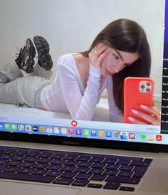 a woman laying on her stomach holding a cell phone in front of a laptop computer