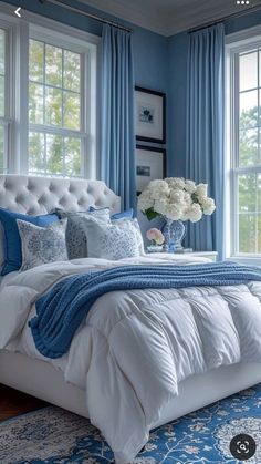 a bedroom with blue walls and white bedding, windows, and rugs on the floor