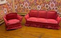 two red couches sitting next to each other on top of a wooden floor in front of a floral wallpaper