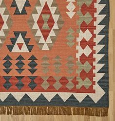 an orange and blue rug with fringes on top of wooden floor next to wall