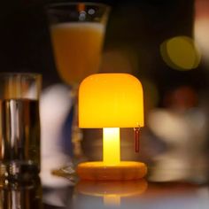 a yellow lamp sitting on top of a table next to two glasses and a drink