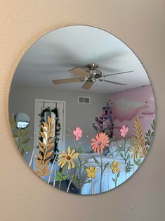 a mirror that has flowers painted on the side of it and a ceiling fan in the background