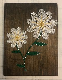 two white flowers with green stems on a wooden board that is decorated with string and beads