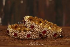 two gold bracelets sitting on top of a wooden table with red stones in the middle