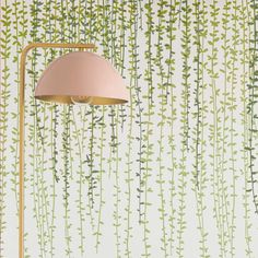 a lamp that is next to a wall with green plants on it and a pink shade