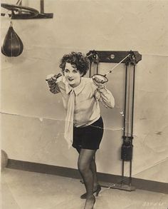 an old black and white photo of a woman holding something in one hand while standing next to a punching bag