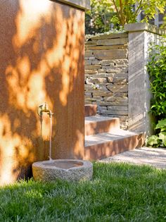 a water fountain sitting in the grass next to a stone wall and steps that lead up to it