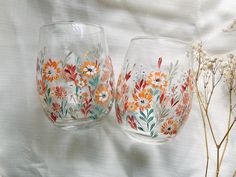 two hand painted wine glasses sitting next to each other on a white surface with flowers