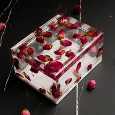 a glass box filled with pink flowers on top of a black table next to petals