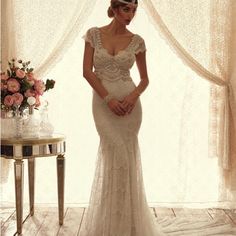 a woman in a wedding dress standing next to a table with flowers and a vase on it