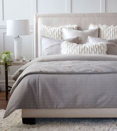 a bed with pillows and blankets on top of it next to a night stand in front of a white wall