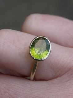 a close up of a person's hand holding a ring with a green stone