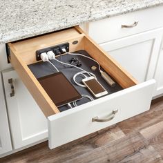 an open drawer in a kitchen with electronic devices and cords on the counter top next to it