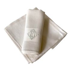 two white napkins sitting on top of each other next to each other with an embroidered monogram