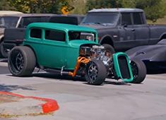 an antique hot rod car driving down the street in front of other classic cars and trucks