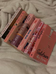 a stack of pink books sitting on top of a white bed covered in fluffy blankets