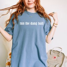 a woman with red hair wearing a blue shirt that says run the dance ball on it