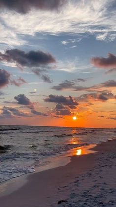 the sun is setting over the ocean with clouds in the sky and sand on the beach