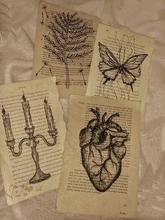 four old book pages with drawings of heart, candle and butterfly on them sitting on a bed