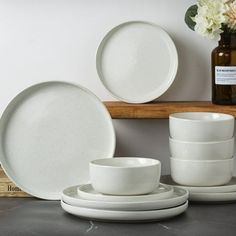 white dishes and cups are sitting on a shelf next to a vase with flowers in it