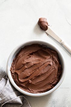 a white bowl filled with chocolate frosting next to a spoon and napkin on a table